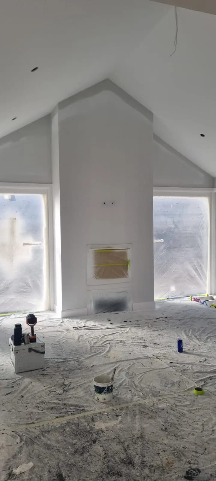 Interior of a new extension with a raked white ceiling and walls, a masked-off fireplace opening in the central chimney breast, and drop sheets covering the floor.